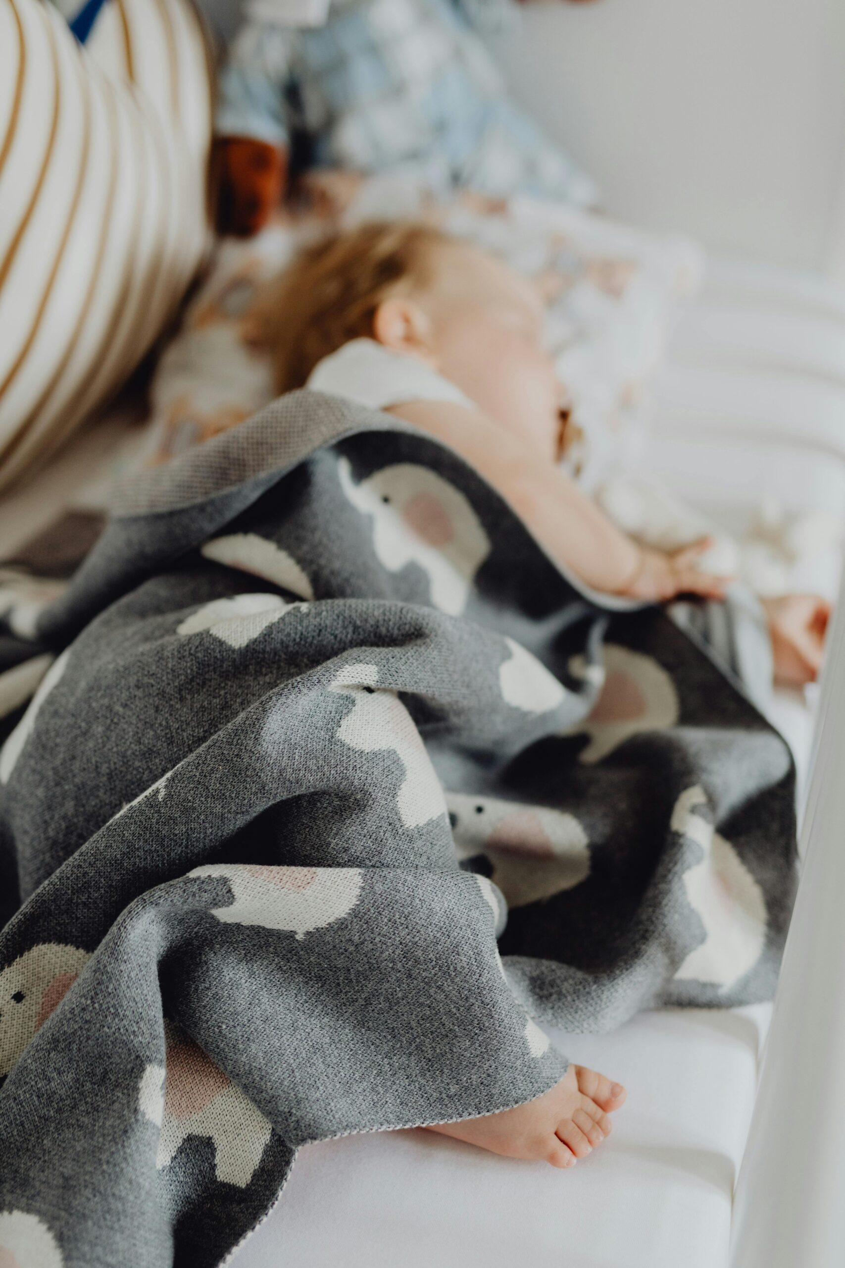 Adorable toddler sleeping soundly under a patterned blanket indoors.